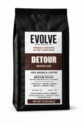 A 12 oz bag of Evolve Bean Coffee Company Detour Mudslide medium roast arabica coffee, shown in a black stand-up bag with a white and dark brown label.